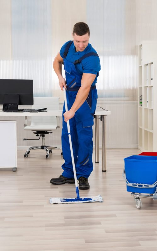 Full length of male janitor mopping floor in office